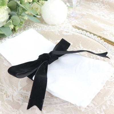 Elegant white napkin tied with a black velvet ribbon on a lace table setting.