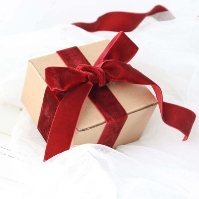 Gift box with red velvet ribbon on soft fabric background.
