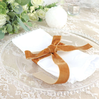 White napkin with brown velvet ribbon on a decorative plate.