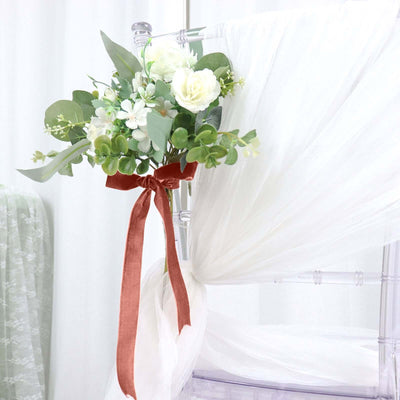 Floral bouquet with greenery and ribbon on a chair draped with white fabric.