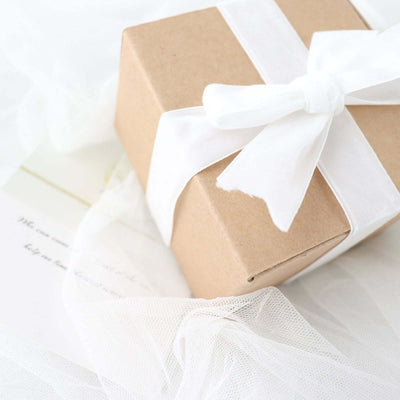 Brown gift box tied with a white ribbon on soft fabric backdrop.