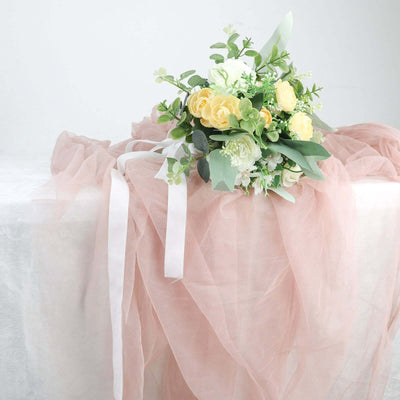 Floral bouquet with yellow roses and greenery on soft pink fabric.