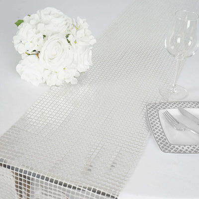 Elegant silver sequin table runner on white table with flowers and glassware.