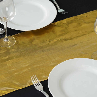 Gold table runner with white plates and glassware on a black table setting.
