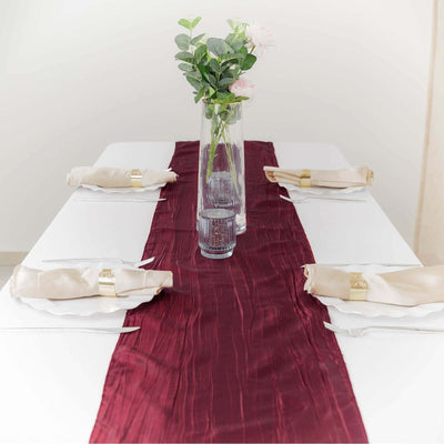 Elegant burgundy table runner with floral centerpiece and napkins on a dining table.