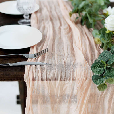 Wrinkled peach table runner on a rustic wooden table with plates and greenery.