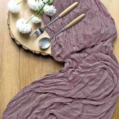 Elegant mauve crinkled fabric draped on a wooden table with cutlery and flowers.