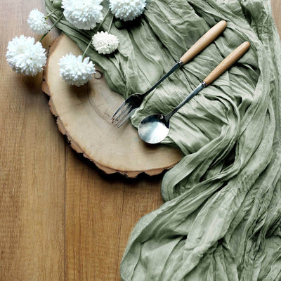 Elegant table setting with green fabric, wooden platter, and silverware.