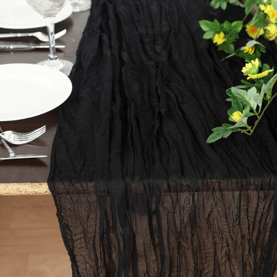 Black crinkled table runner on a wooden dining table with floral decor.