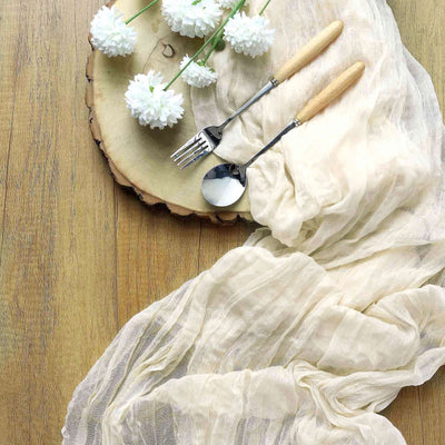 Elegant table setting with soft fabric, utensils, and flowers on a wooden surface.