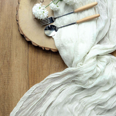 White textured fabric draped on a wooden surface with cutlery and flowers.