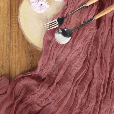 Textured mauve table runner with wooden serving utensils on a rustic wooden surface.