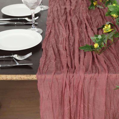 Crinkled rose table runner on a dining table with plates and cutlery.