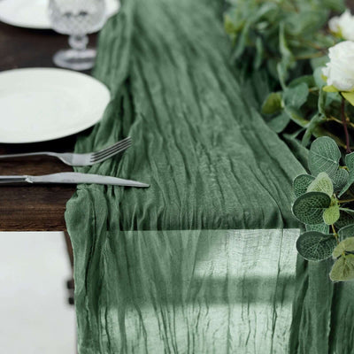 Green textured table runner on a rustic wooden table with plates and greenery.