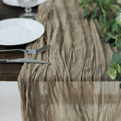 Textured beige table runner draped on a wooden table with plates and greenery.