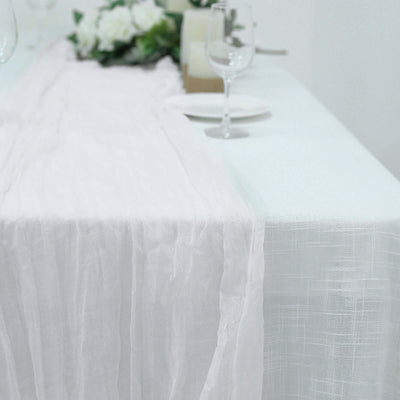 White table runner on a dining table with glassware and floral decor.