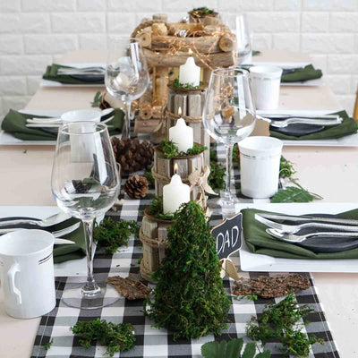 Rustic table setting with candles, greenery, and pine cones for a cozy atmosphere.