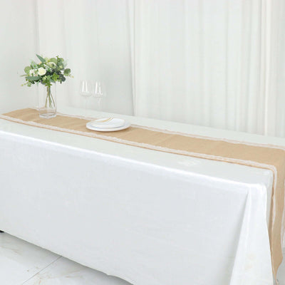Elegant burlap table runner on a white table setting with flowers and dinnerware.
