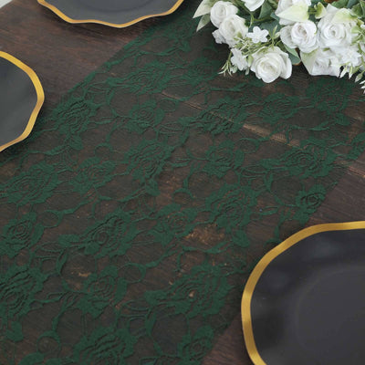 Green lace table runner on a wooden table with black plates and white floral arrangement.