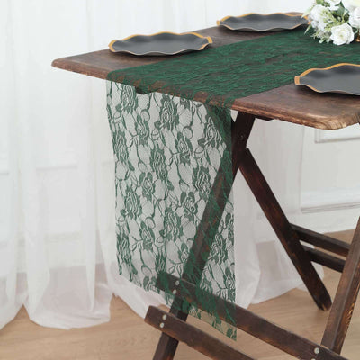 Green lace table runner on a wooden table with black plates and floral centerpiece.
