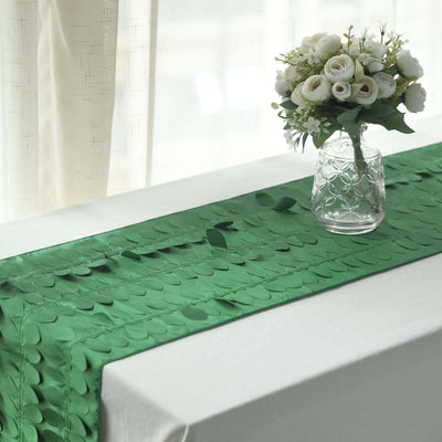 Green leaf-patterned table runner with a vase of white flowers on a table.