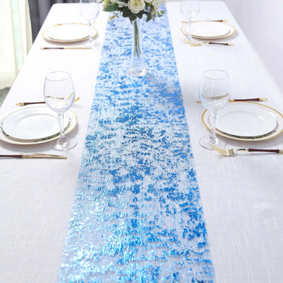 Blue sequined table runner on a white table setting with plates and glasses.