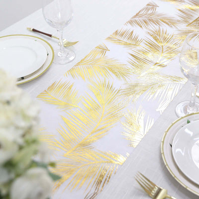 Gold palm leaf table runner on a white table setting with plates and glasses.