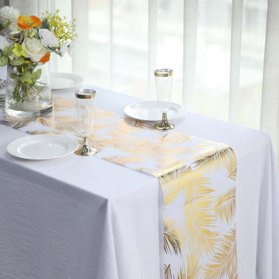 Gold leaf palm table runner on a white table setting with plates and glasses.
