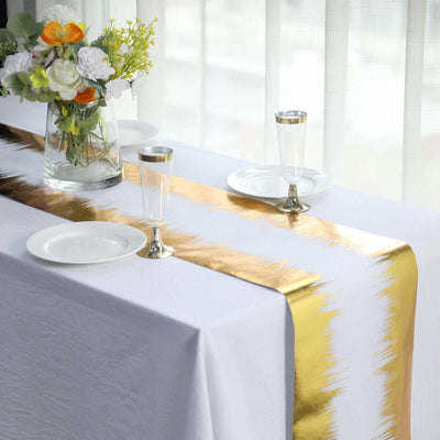 Gold striped table runner on a white table with elegant glassware and floral arrangement.