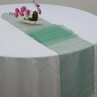 Green sheer table runner on a white table with decorative flowers.