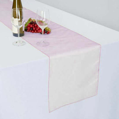 Elegant table runner with wine, glasses, and grapes on a white table.
