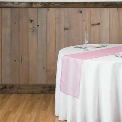 Table set with a white tablecloth and pink runner against a wooden wall.