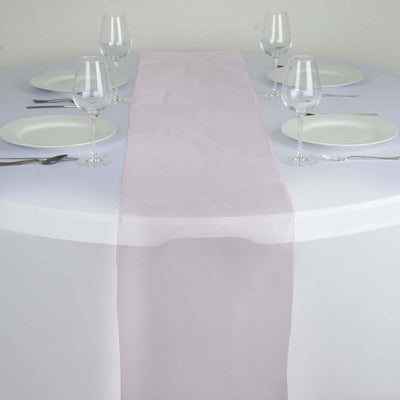 Pink table runner on a round dining table set with plates and glasses.