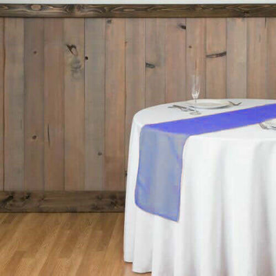 Table set for dining with a white tablecloth and purple runner against a wooden wall.