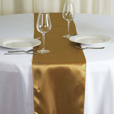 Gold satin table runner on a white table with plates and glasses.