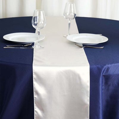 Elegant satin table runner on a navy tablecloth with plates and glasses.