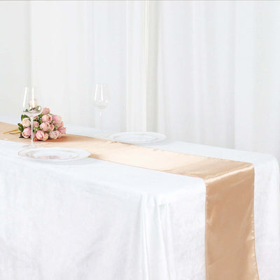Elegant champagne satin table runner on a white table with floral arrangement.