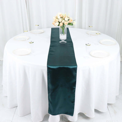 Teal satin table runner on a round white table with floral centerpiece.