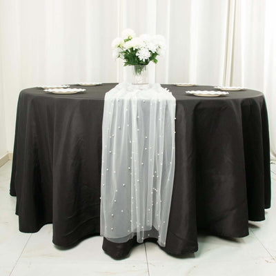 Black round table with white floral centerpiece and sheer table runner.