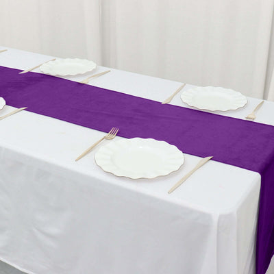Purple table runner with white plates and utensils on a dining table.
