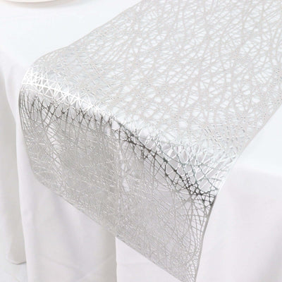 Silver lace table runner with intricate design on a white table.