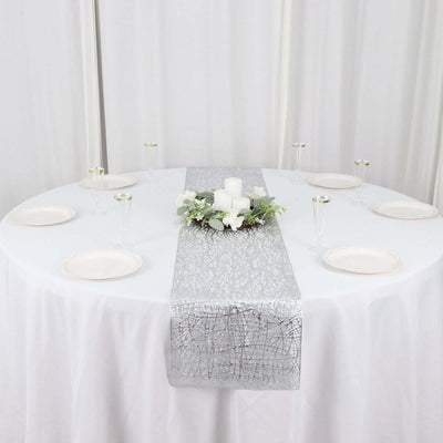 Elegant silver table runner on a round table with candles and floral decor.