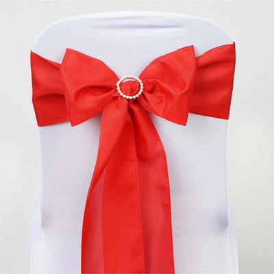 Red satin chair sash bow with pearl embellishment on a white chair.