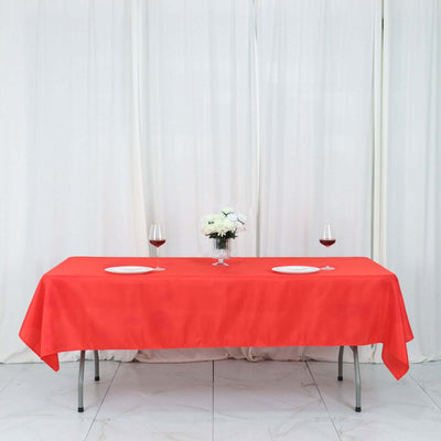 Red tablecloth set for dining with glasses and flowers on a white backdrop.
