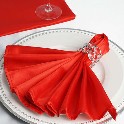 Red satin napkin elegantly folded on a decorative plate with a jeweled napkin ring.