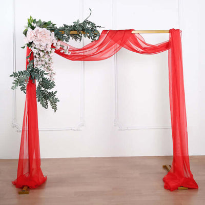 Red wedding arch adorned with flowers and draped fabric on a plain backdrop.
