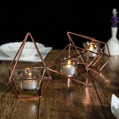 Geometric copper candle holders with glass tea light candles on a wooden table.