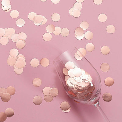 Rose gold confetti scattered around an empty glass on a pink background.