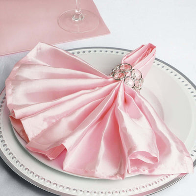 Elegant pink satin napkin draped on a plate with a decorative napkin ring.