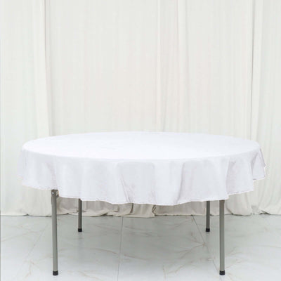 Round white table with a tablecloth on a plain backdrop.